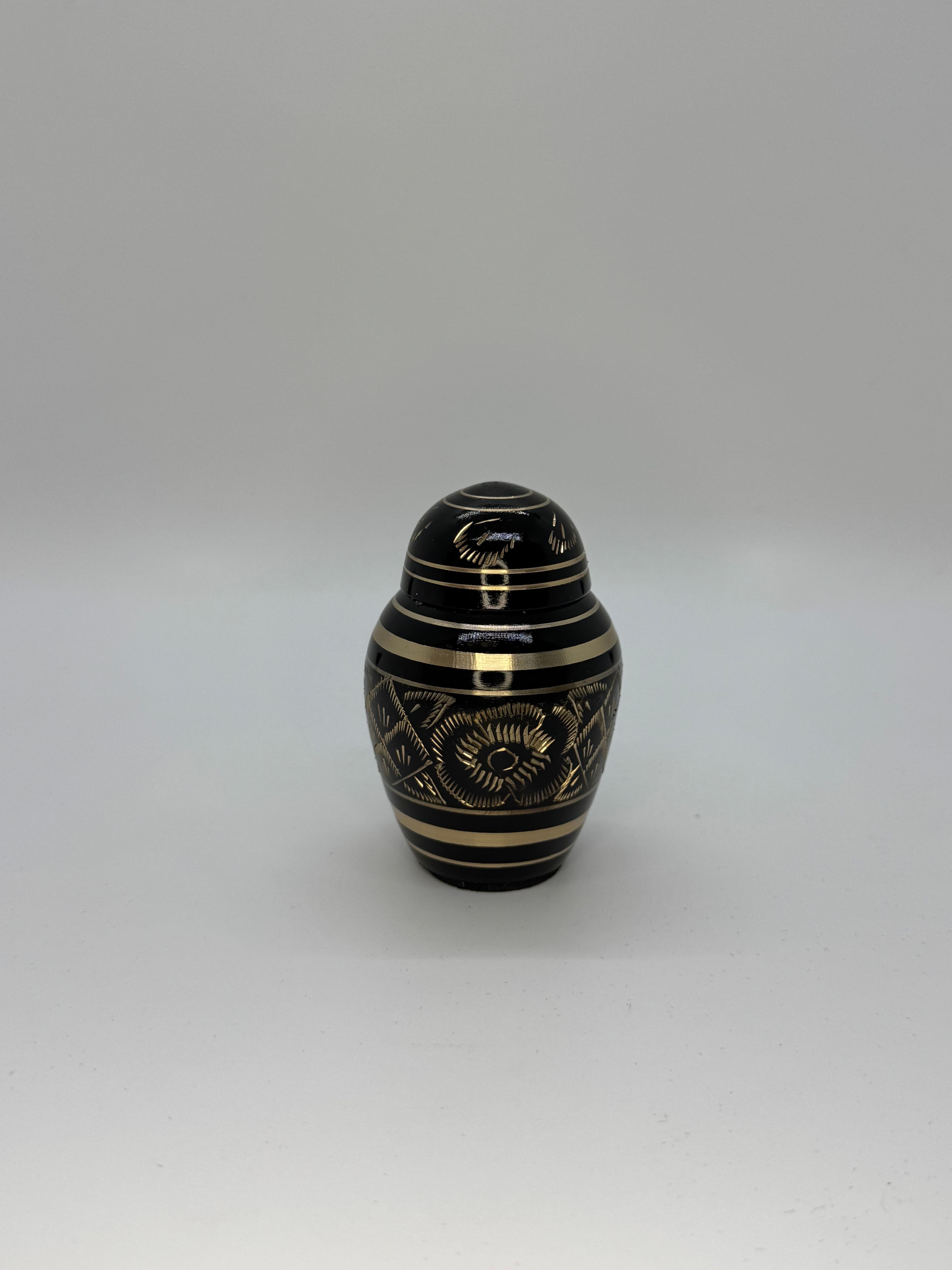 Black metal keepsake urn with gold color engraving embellishments featuring a domed top.